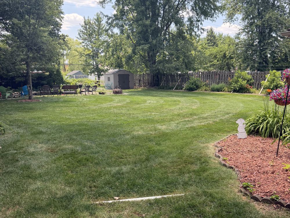 A freshly mowed backyard lawn with a mulch bed border and seating area in Macomb County