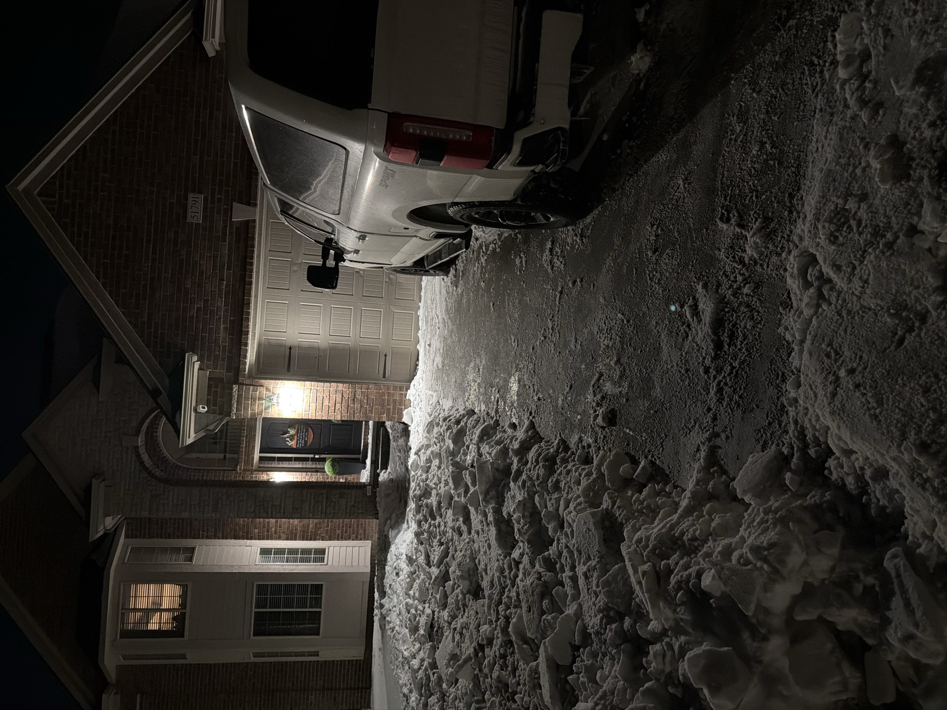 Summit Snow and Lawn crew clearing a walkway beside a truck during a night snowfall in Macomb County